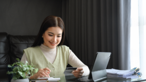 Attractive young woman holding credit card and calculating monthly expenses at home.