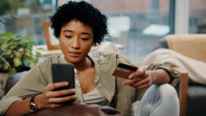 Shot of a young woman holding her credit card while using her cellphone at home