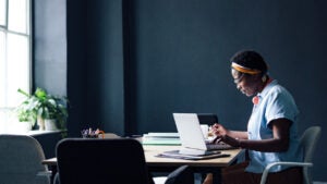 Young Black woman sits at table looking at laptop with a pensive expression.