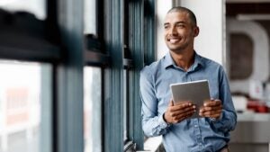 Shot of a young businessman using a digital tablet while standing at a window in an office