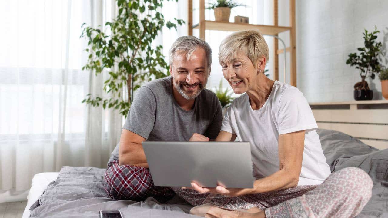 Senior couple lounges in bed in pyjamas, planning for the week ahead