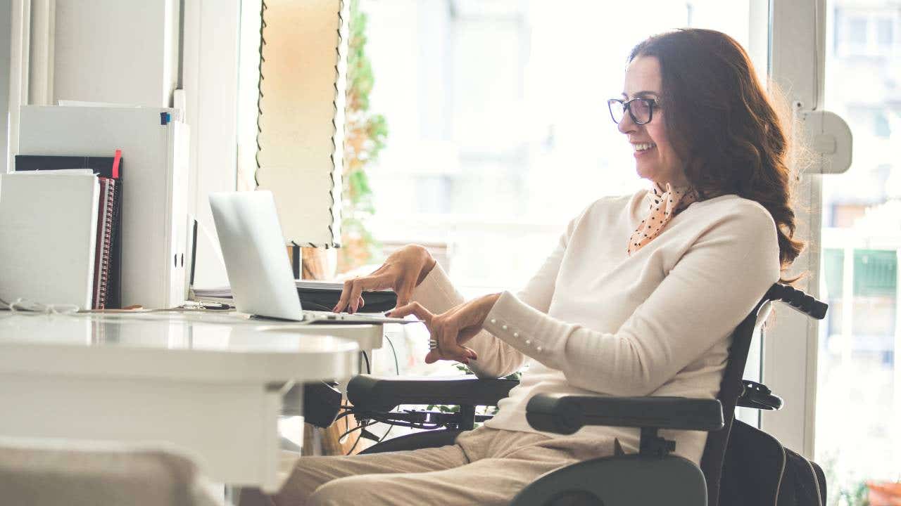 Side view of a happy woman with physical disability working on a laptop in the office.