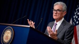 Federal Reserve Chair Jerome Powell speaking at a podium with an American flag in the background.