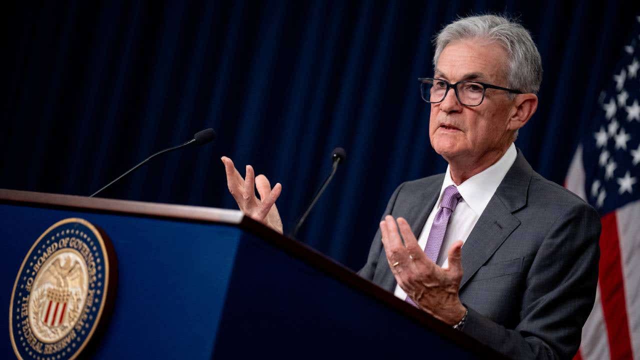 Federal Reserve Chair Jerome Powell speaking at a podium with an American flag in the background.