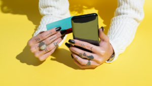 Woman's Hands using credit card for shopping online on her smartphone Over Yellow Background