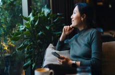 woman with smartphone looking out through window while sitting in a cafe having coffee