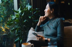 woman with smartphone looking out through window while sitting in a cafe having coffee