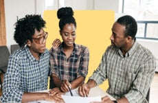 A Black couple and loan underwriter look at a contract.