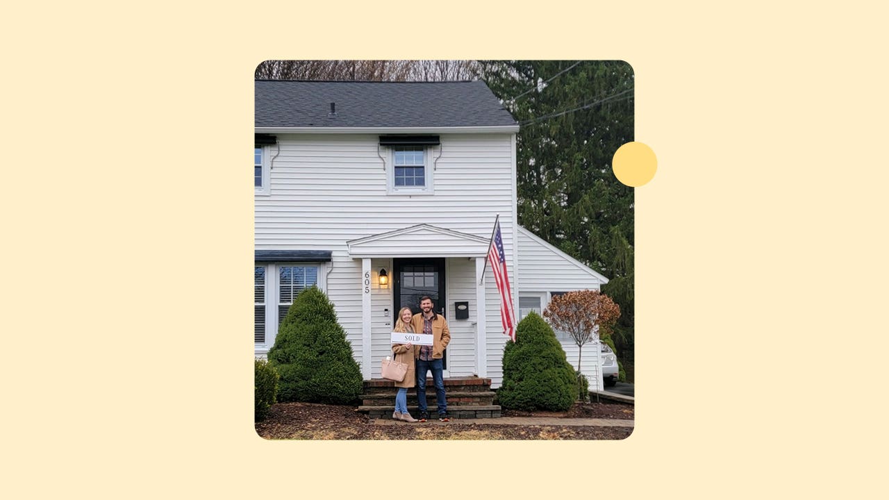 Happy homebuyers standing in front of their new home holding a "SOLD" sign