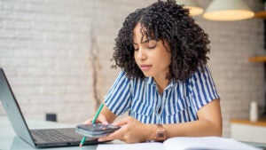 Woman using calculator and working on laptop