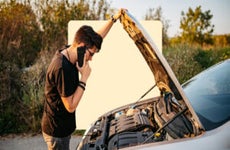 Person looking under hood of car while on phone