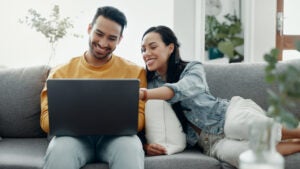 Couple sitting on a sofa, looking at a laptop