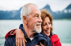 Couple standing on a dock with an out-of-focus body of water behind them.