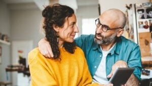 Couple smiling at each other while looking at something on a tablet computer.