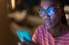 Person looking at smartphone with stock charts on the phone's screen reflecting in their eyeglasses.