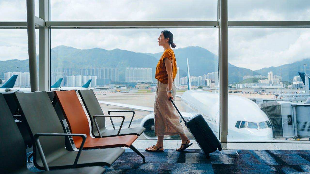 woman carrying suitcase, walking by the window at airport terminal