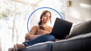 a woman sits on her couch with her laptop