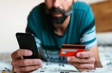 Close up hand holding credit card and shopping online on bed