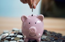 Person Putting Coin In Piggy Bank At Table