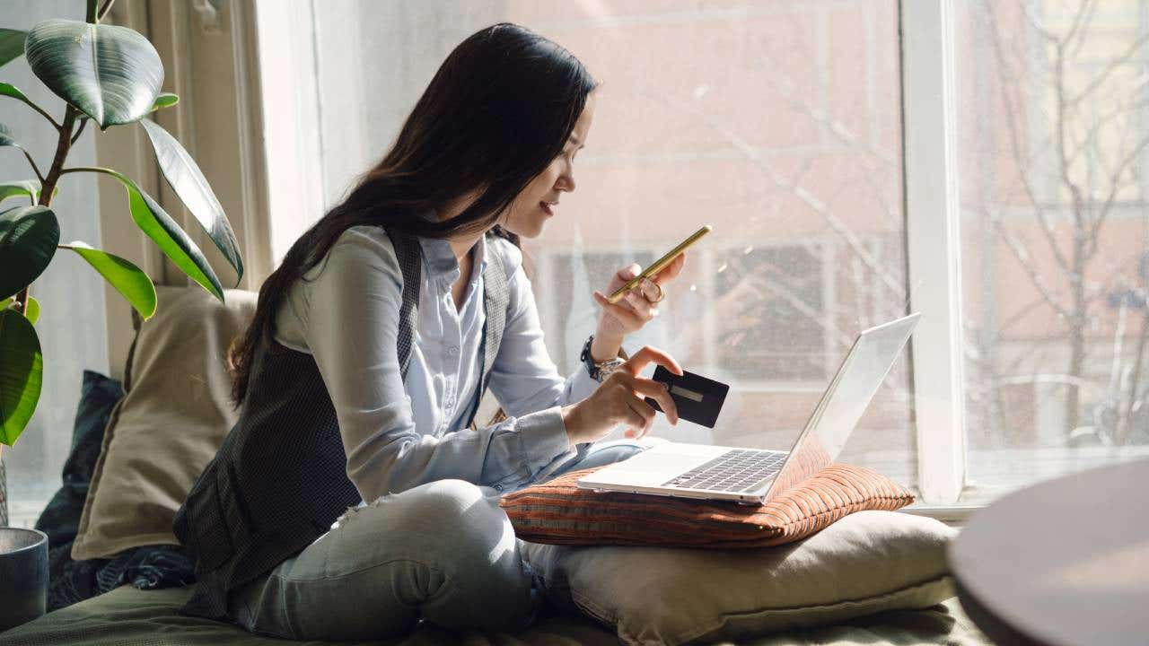 Woman in blue jeans sitting on the bed in a yoga pose in front of a laptop