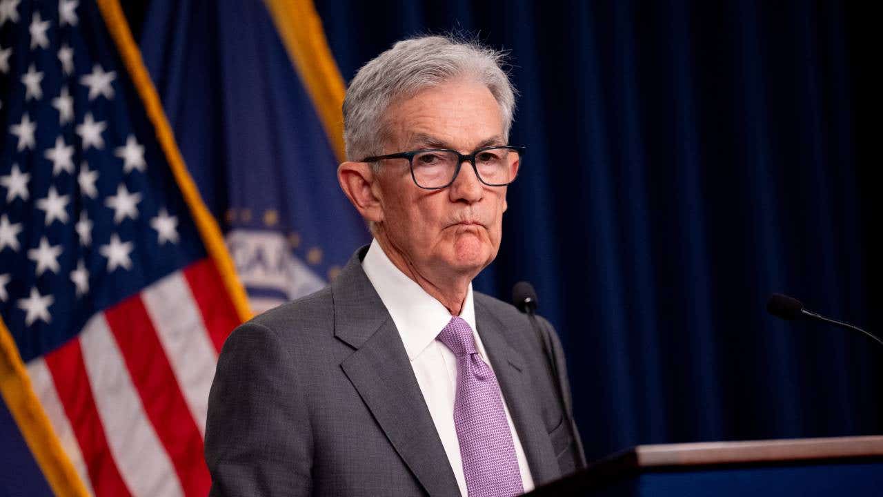 Federal Reserve Chair Jerome Powell standing at a lectern with an American flag in the background.