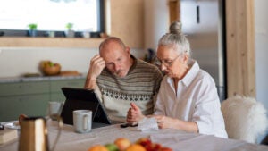 Senior couple sitting at the kitchen table looking at digital tablet and recalculating their expenses.