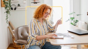 Red haired woman reading bill at desk.