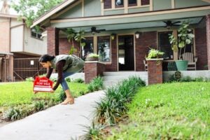 realtor placing red for sale sign outside craftsman style house