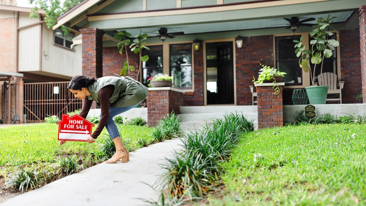 realtor placing red for sale sign outside craftsman style house