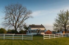 white farmhouse exterior with green land and white fence