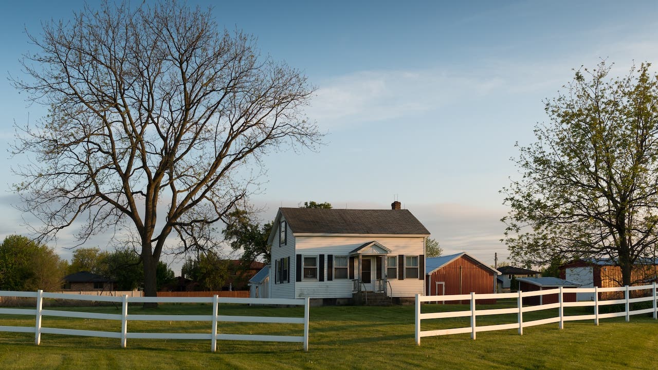 white farmhouse exterior with green land and white fence