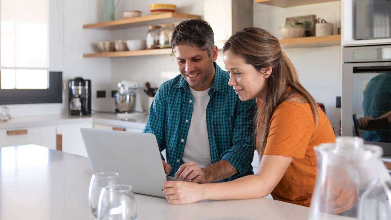 Two people in a kitchen looking at a laptop.