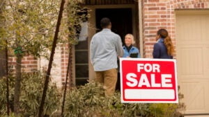 3 people standing with a "For Sale" sign in the foreground