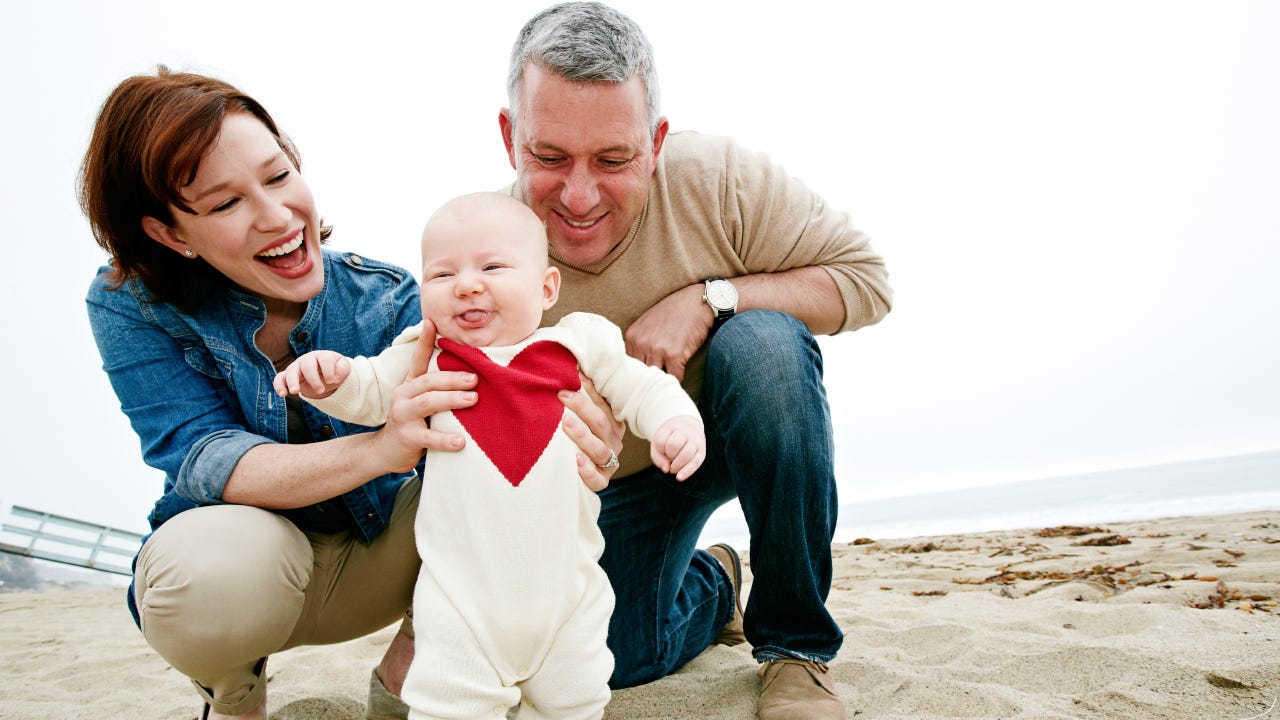 Parents helping baby walk on beach