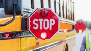 School bus with attached STOP sign extended and a bus monitor partially in the frame walking by the side of the bus