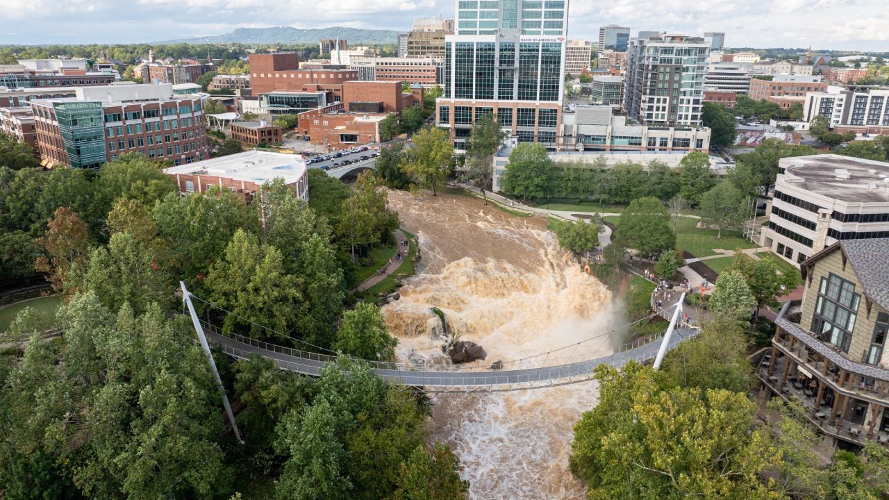 The Liberty Bridge stretches across the roaring Reedy River in Greenville, SC, as floodwaters churn below.