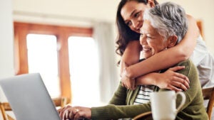 A young woman hugging her grandmother before helping her with her finances on a laptop.