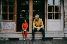 Portrait of Japanese grandfather and cute preschool granddaughter sitting on patio and smiling at each other