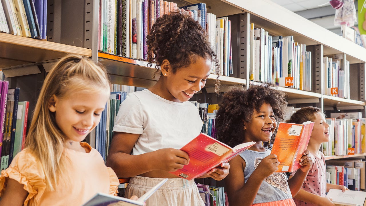 Four girls read books in a library.