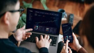 Two people looking at stock charts on a smartphone and a laptop.