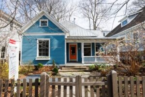 blue house with white trim and porch, wood fence and for sale sign in front yard