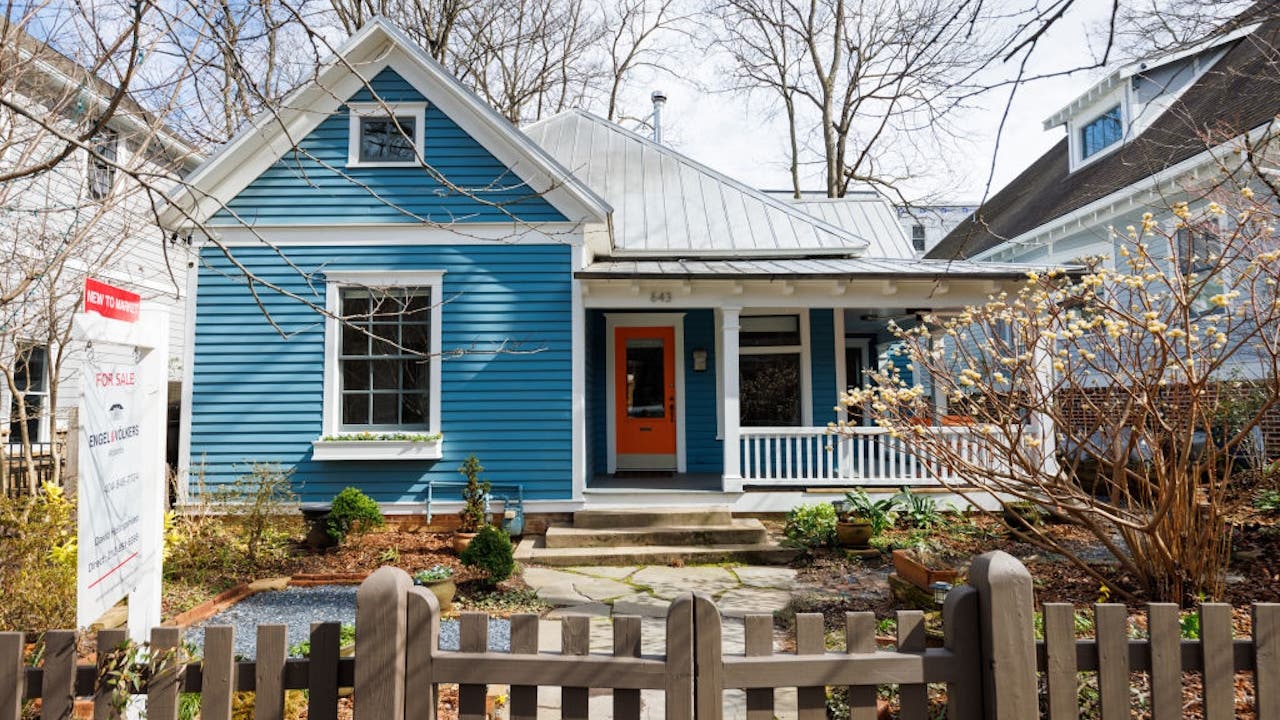 blue house with white trim and porch, wood fence and for sale sign in front yard