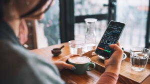 A woman uses a smartphone buy cryptocurrency at a coffee shop while drinking a latte.