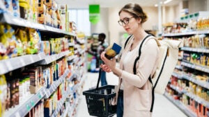 A woman reading the label on a food item while out shopping for groceries in her local supermarket.