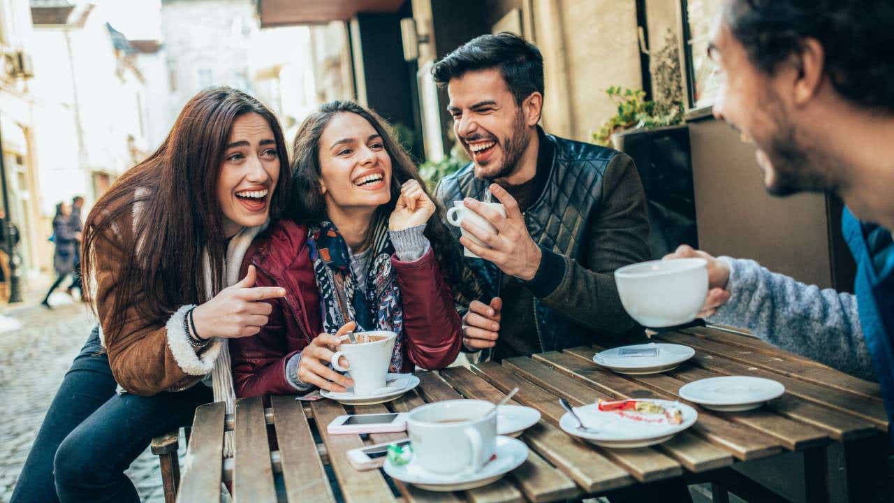 Group of friends laughing around a table drinking coffee.