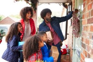 african-american family knocking on front door of suburban house decorated for christmas