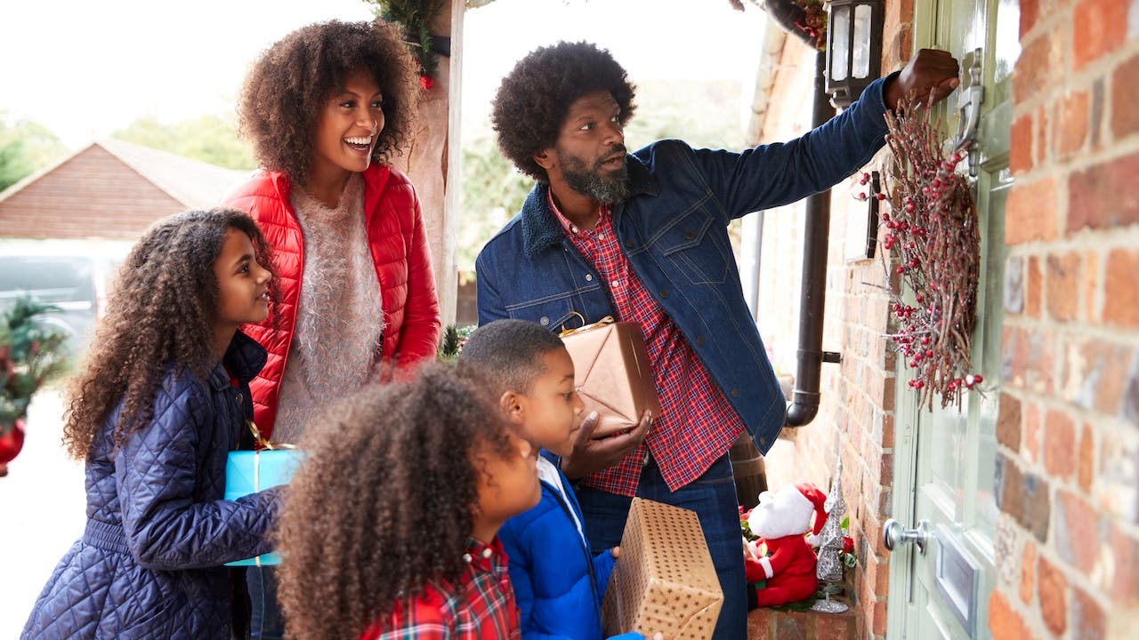 african-american family knocking on front door of suburban house decorated for christmas