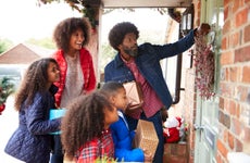 african-american family knocking on front door of suburban house decorated for christmas