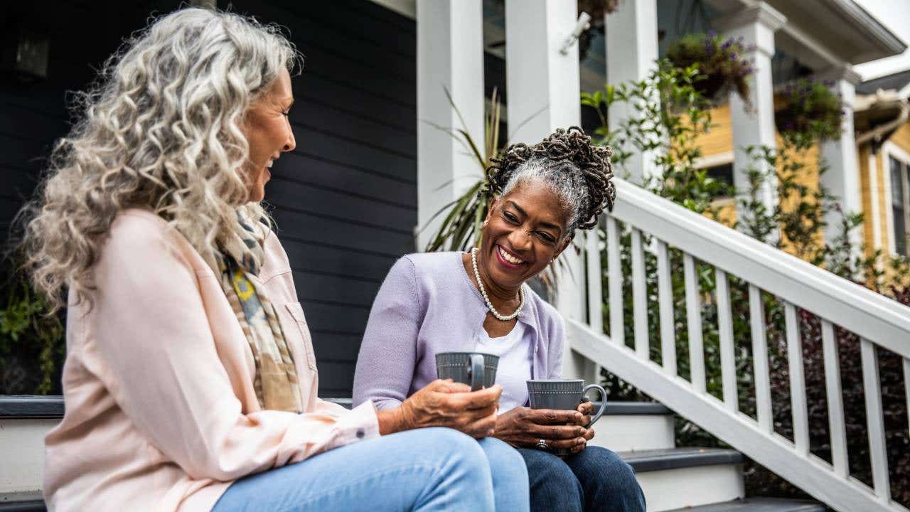 Older women drink coffee in front of a suburban house.