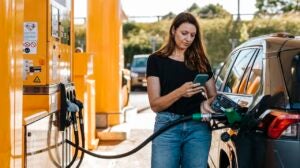 Woman using smart phone while refueling car at gas station